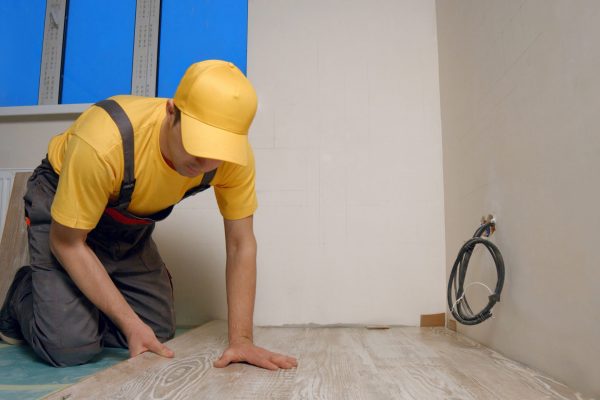 Skilled master laying laminate floor in apartment. Construction worker is engaged in laying laminate in the room. Repair and finishing work.